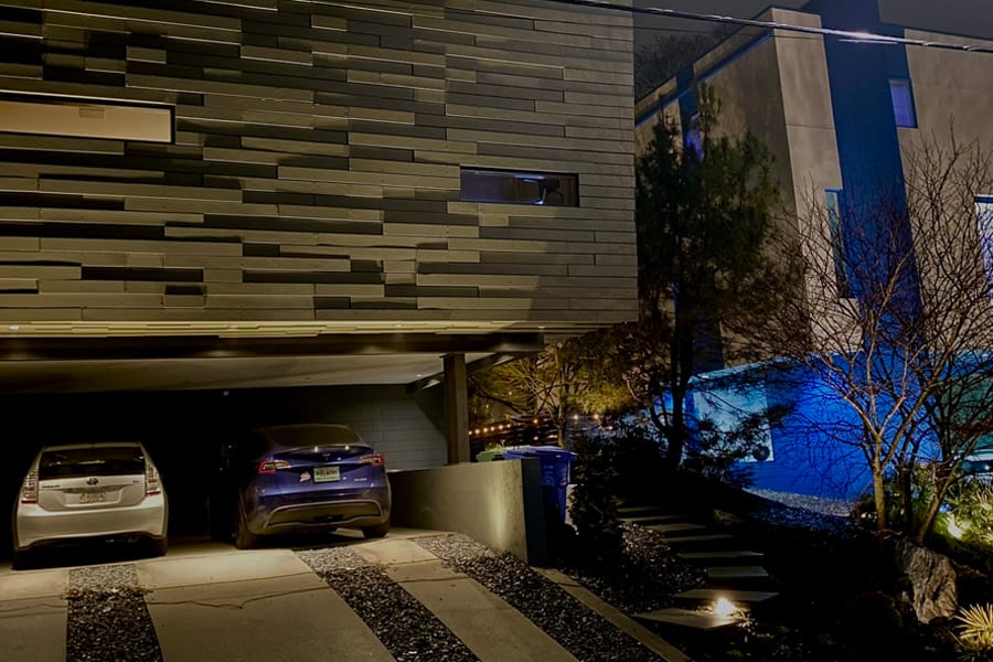 Modern house at night with two cars parked in a driveway, surrounded by minimalistic landscaping. Soft lighting and blue pool hues create a serene atmosphere.